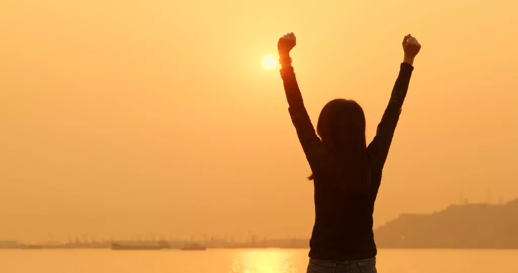 The silhouette of a woman with her arms in the air, celebrating, against an orange sunset