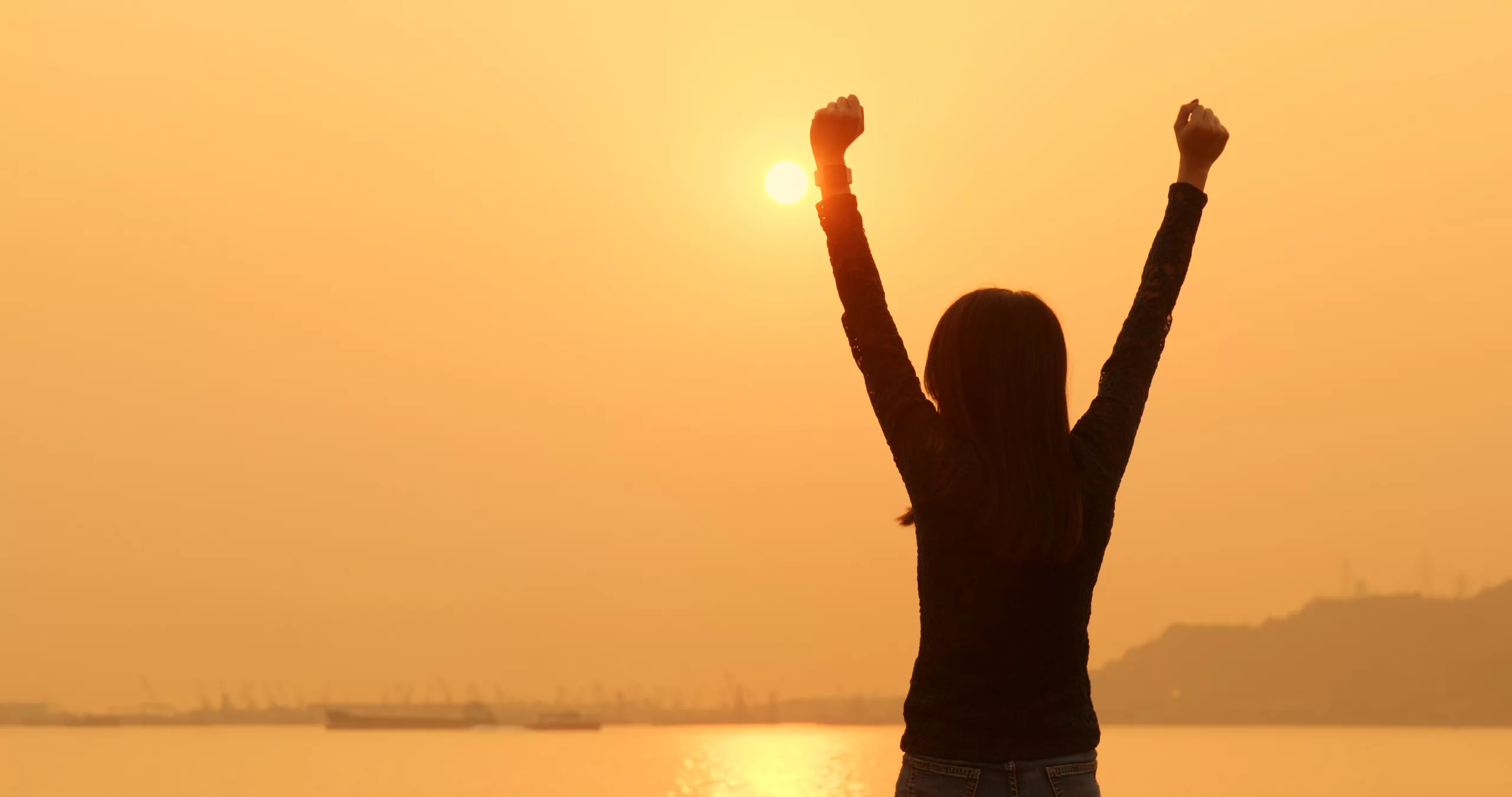 The silhouette of a woman with her arms in the air, celebrating, against an orange sunset