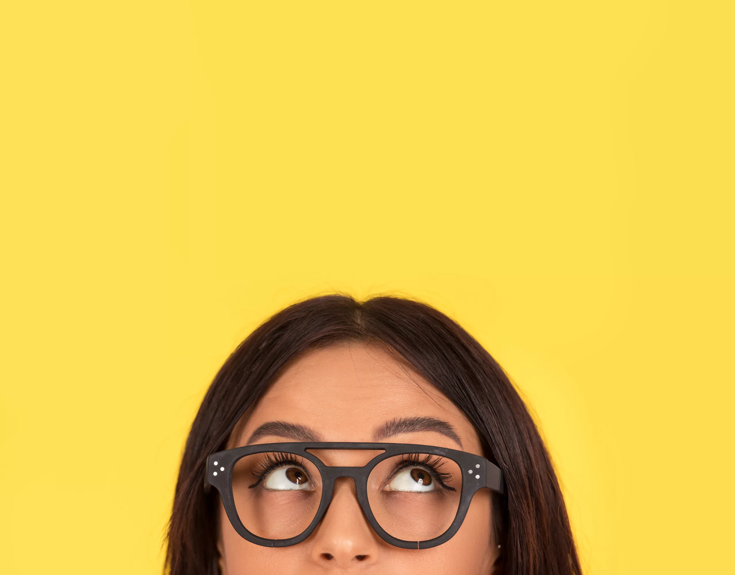 The top half of the face of an Indian woman wearing glasses is visible at the bottom of the image. She is standing against a yellow background and looking up and to the right.